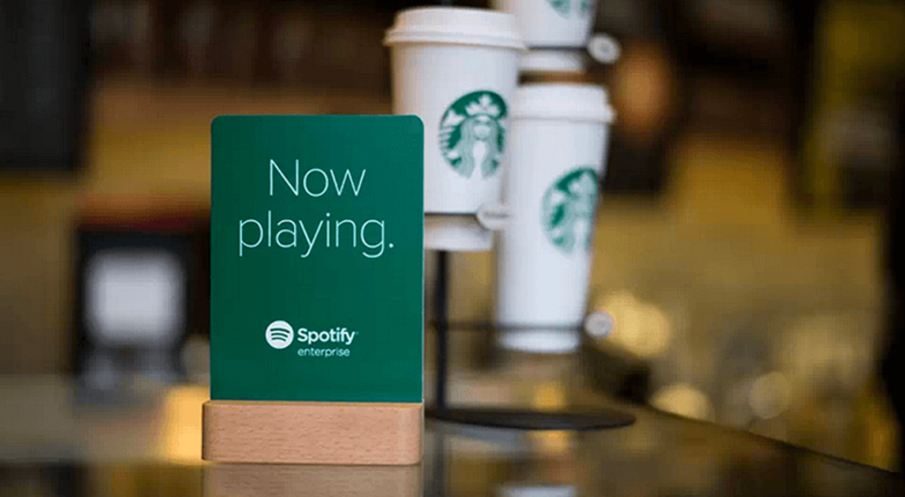 Starbucks cups table-top sign that says "Now playing." on a Spotify-branded background.