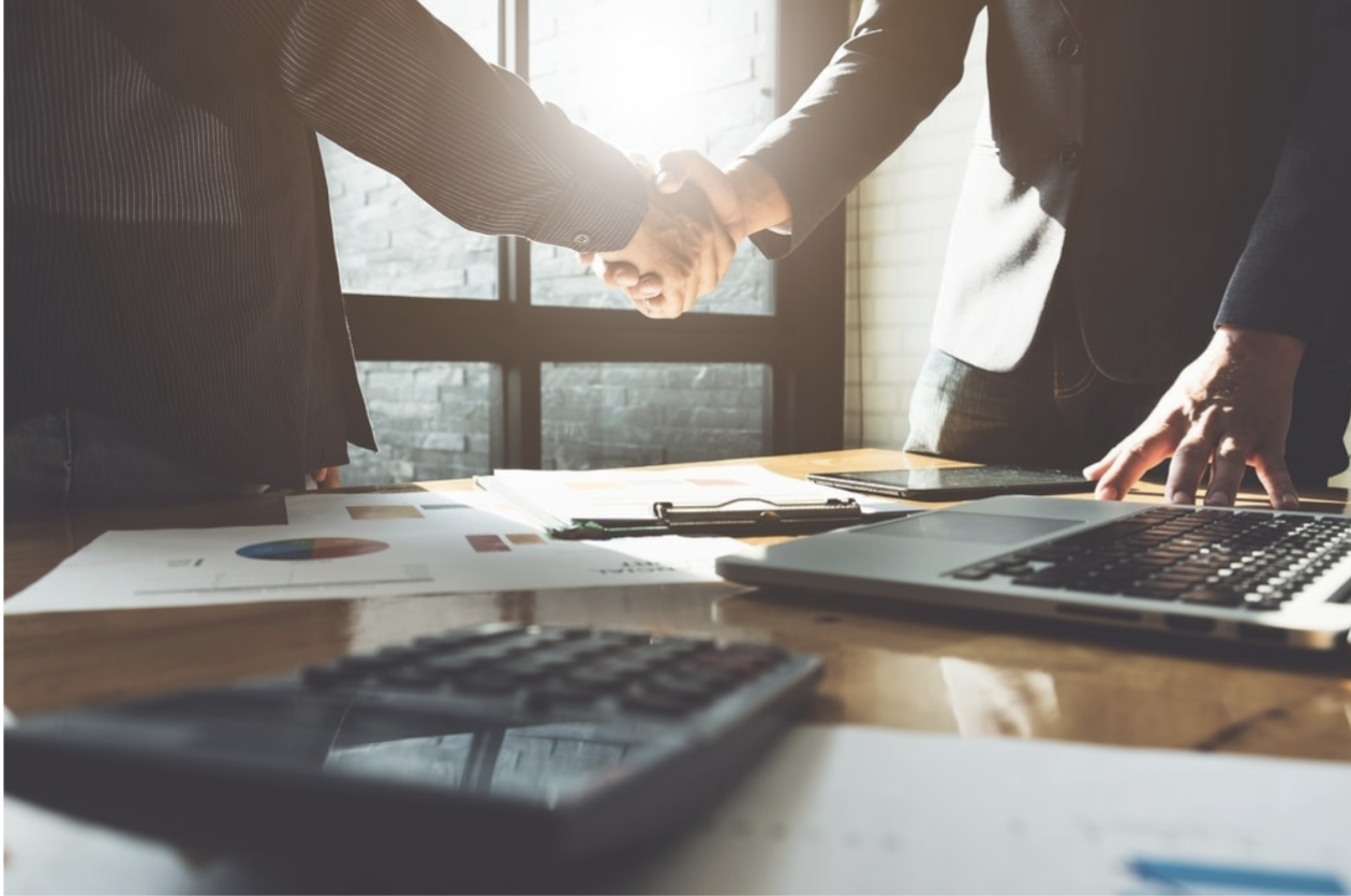 Two professionals shaking hands over a desk, symbolizing collaboration.